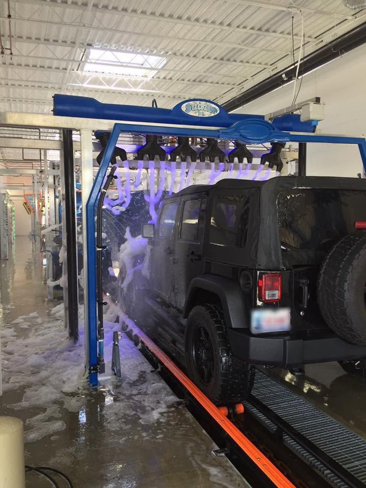 Black Jeep rolling under a foam arch on the conveyor inside the wash tunnel