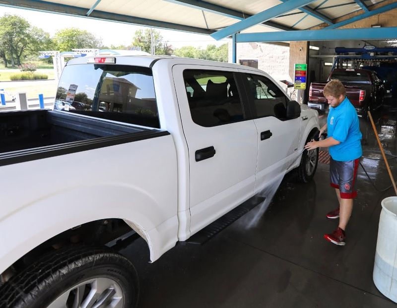 Fast Wash crew member pressure-rinsing the side of a white pickup at the tunnel entrance