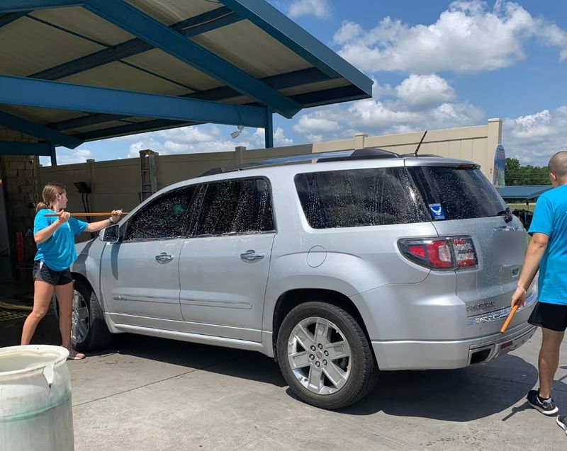 Two Fast Wash crew members scrubbing a silver SUV before it enters the tunnel