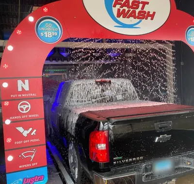 Black Chevy Silverado covered in foam under the red Fast Wash entrance arch