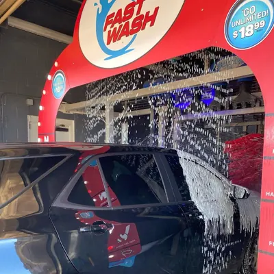 Black SUV entering the red Fast Wash arch as water sprays inside the tunnel